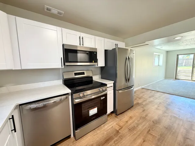Modern kitchen featuring white shaker cabinetry, stainless steel appliances, light-toned countertops, and wood-finish flooring