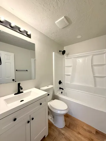Full bathroom featuring a white vanity with integrated sink, matte black fixtures, a white toilet, and a white tub with shower surround