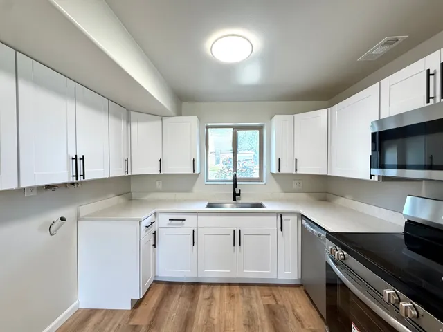 Kitchen featuring white shaker cabinetry, light-toned countertops, wood-finish flooring, a stainless steel appliance suite, and a black matte faucet