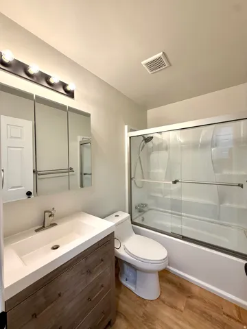 Bathroom featuring a wood-finish vanity with an integrated sink, tri-panel mirrored medicine cabinet, brushed nickel faucet, and a combination tub/shower with sliding glass doors