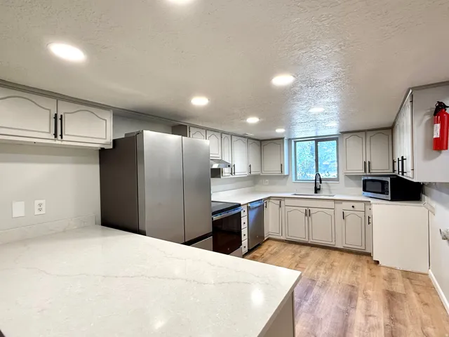 Kitchen featuring light wood-finish flooring, white cabinetry with black hardware, and light-toned countertops