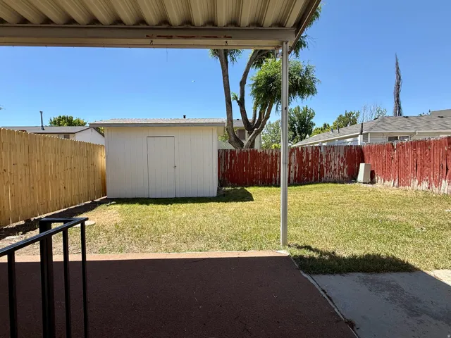 Covered patio area opening to a fenced backyard featuring a storage shed and grass