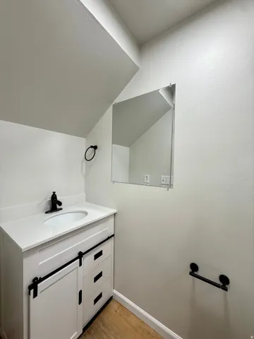 Bathroom vanity with a white countertop and oval sink, matte black faucet, and barn-door style cabinetry