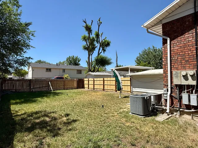 Expansive backyard featuring a partial wood fence, mature tree, and a red brick exterior with white gutters