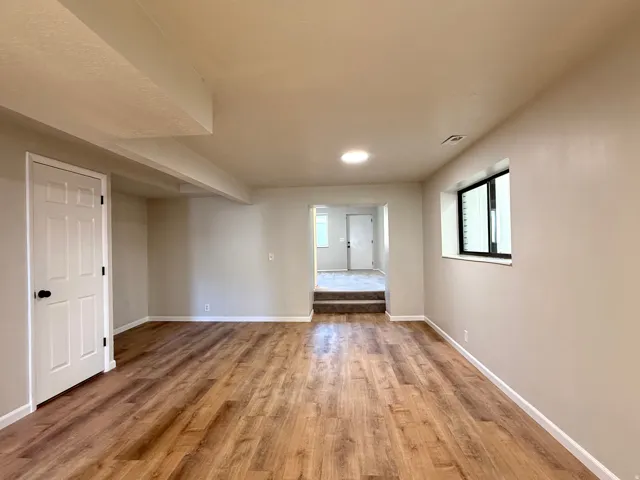 Spacious room featuring wood-finish flooring, neutral wall tones, recessed lighting, a white paneled door, and a black-framed window