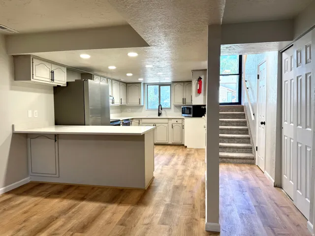 Kitchen featuring light-toned cabinetry, a spacious white countertop, stainless steel refrigerator, and wood-finish flooring