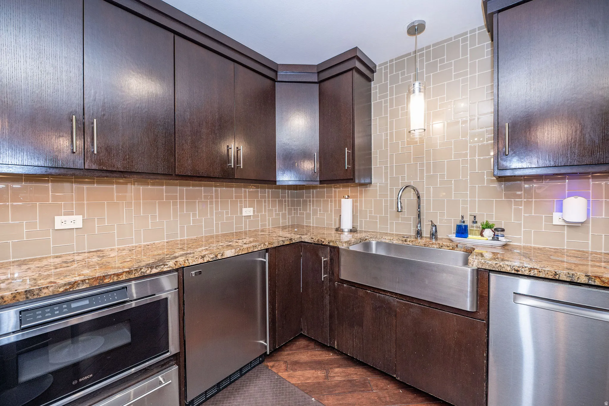 Kitchen featuring dark wood cabinetry, light-toned tile backsplash, and stone countertops