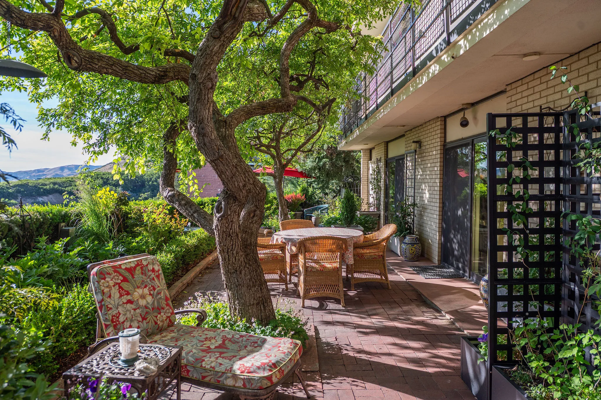 Private brick paver patio area featuring mature trees, lush perimeter landscaping, and a white brick exterior