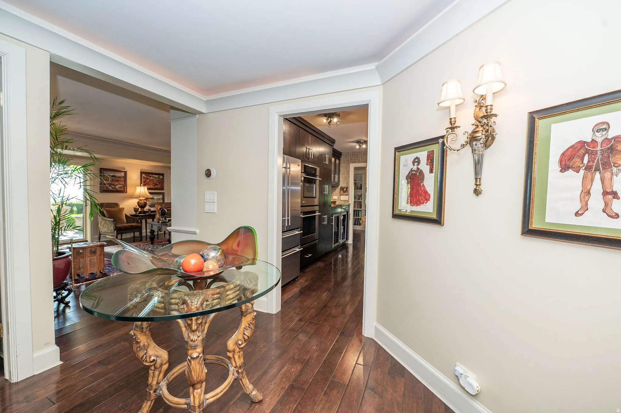 Hardwood flooring extending through multiple rooms, elegant wall sconce lighting, and classic crown molding