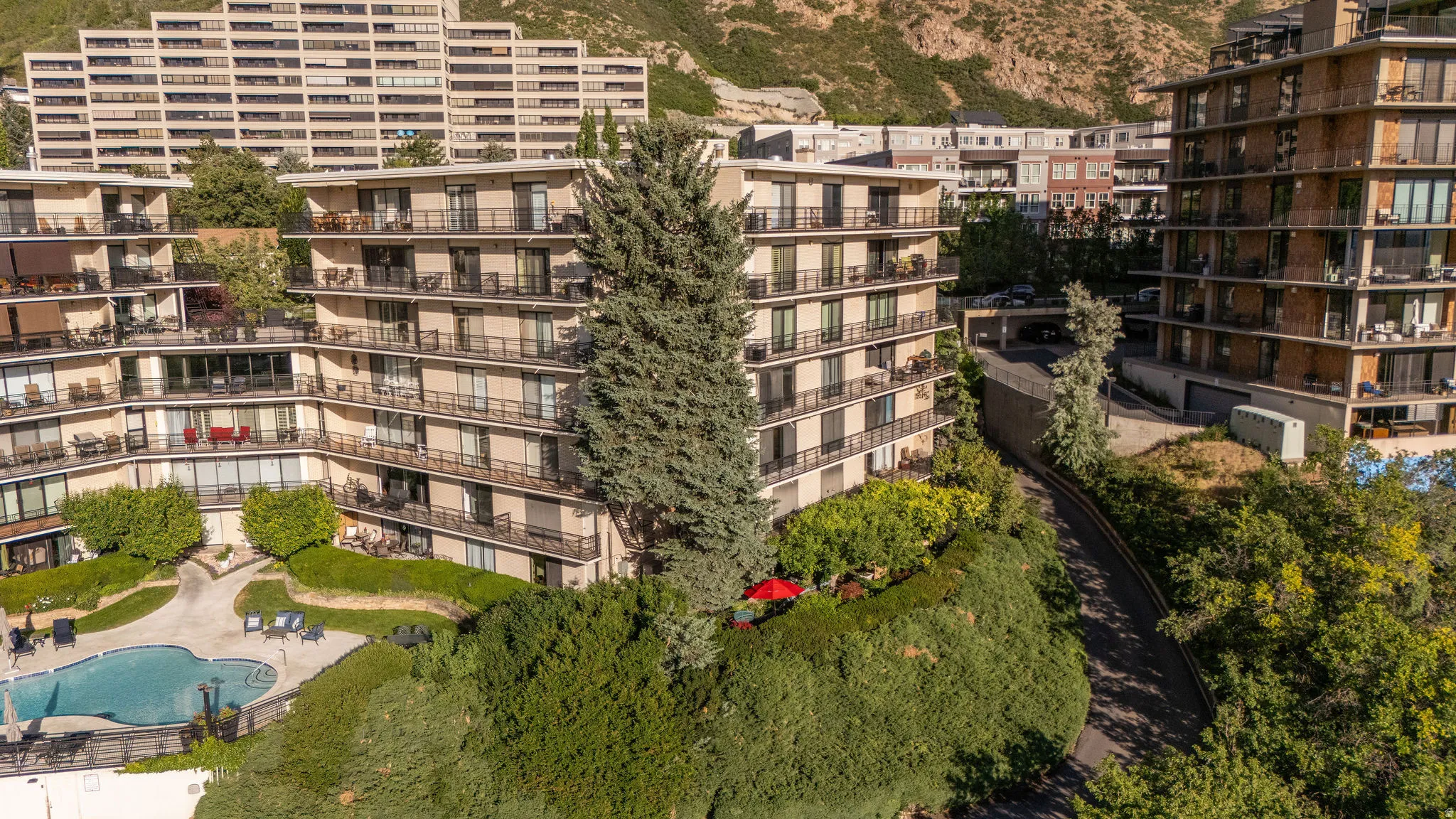 Multi-story building featuring balconies, terraced landscaping, a lower-level swimming pool, and mountain backdrop