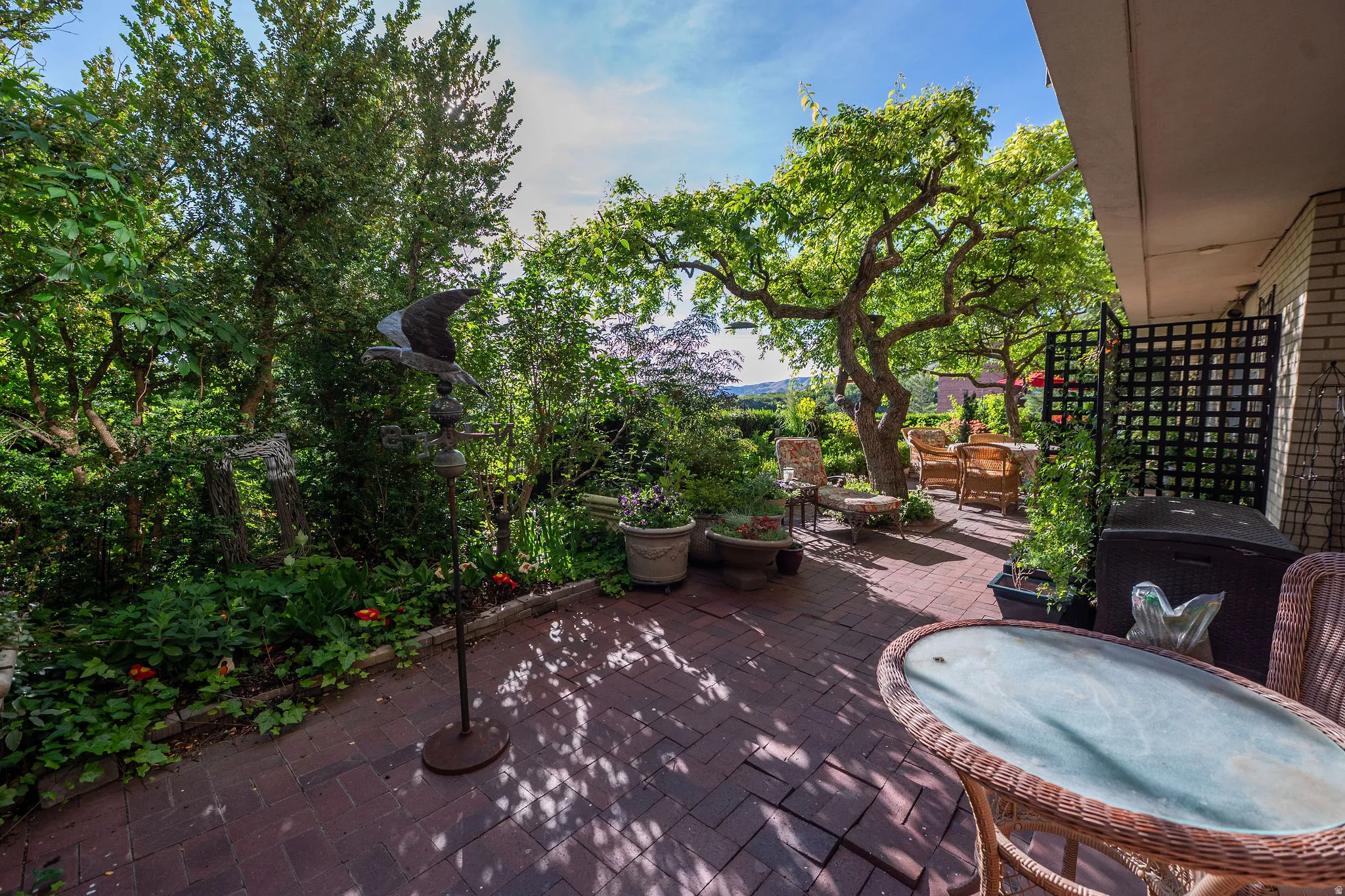 Expansive brick paver patio featuring mature trees, surrounding lush greenery, and a lattice privacy screen