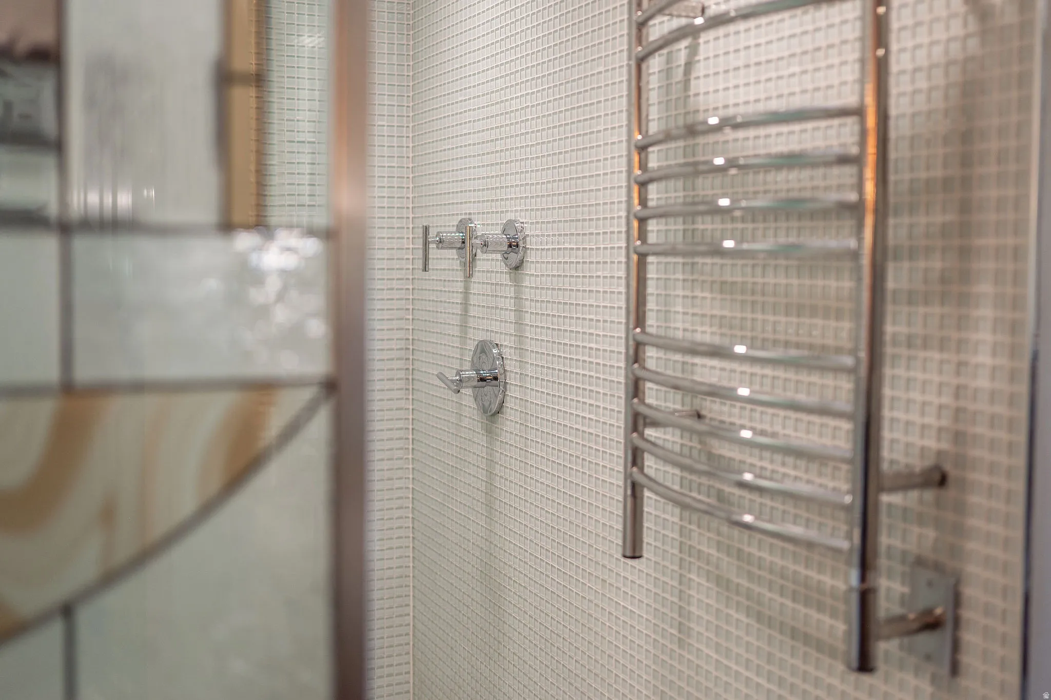 Chrome towel warmer mounted on a grid-patterned tile wall