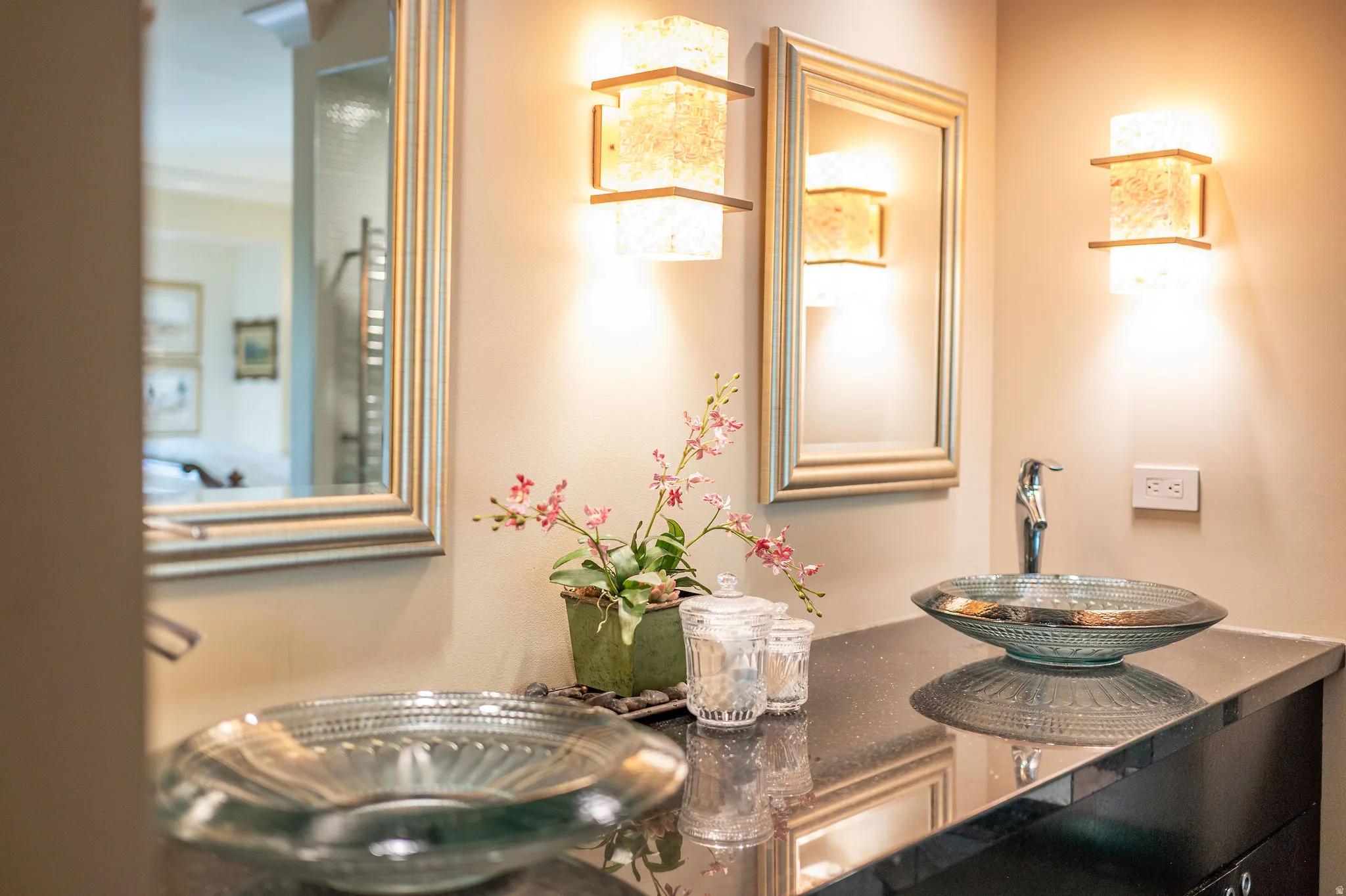 Vanity area featuring dual vessel sinks, wall-mounted sconces, and framed mirrors