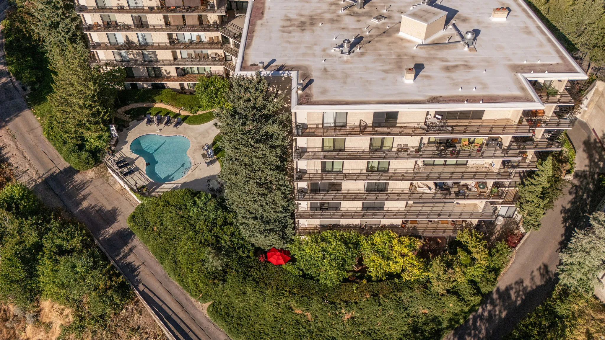 Multi-story building featuring numerous private balconies, a rooftop with mechanical units, and a ground-level swimming pool with surrounding patio