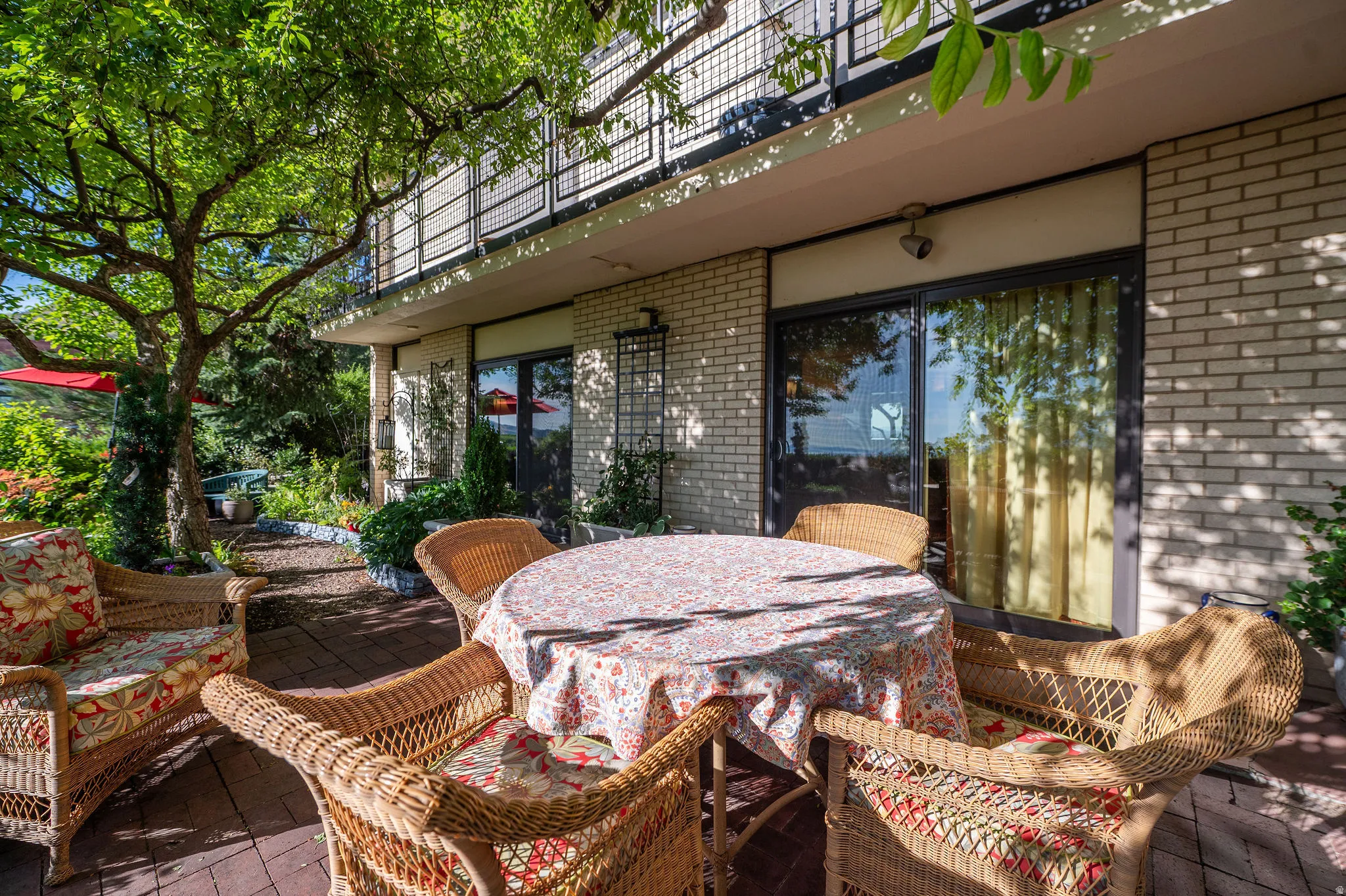Expansive outdoor patio featuring brick pavers, mature tree for natural shade, and brick exterior