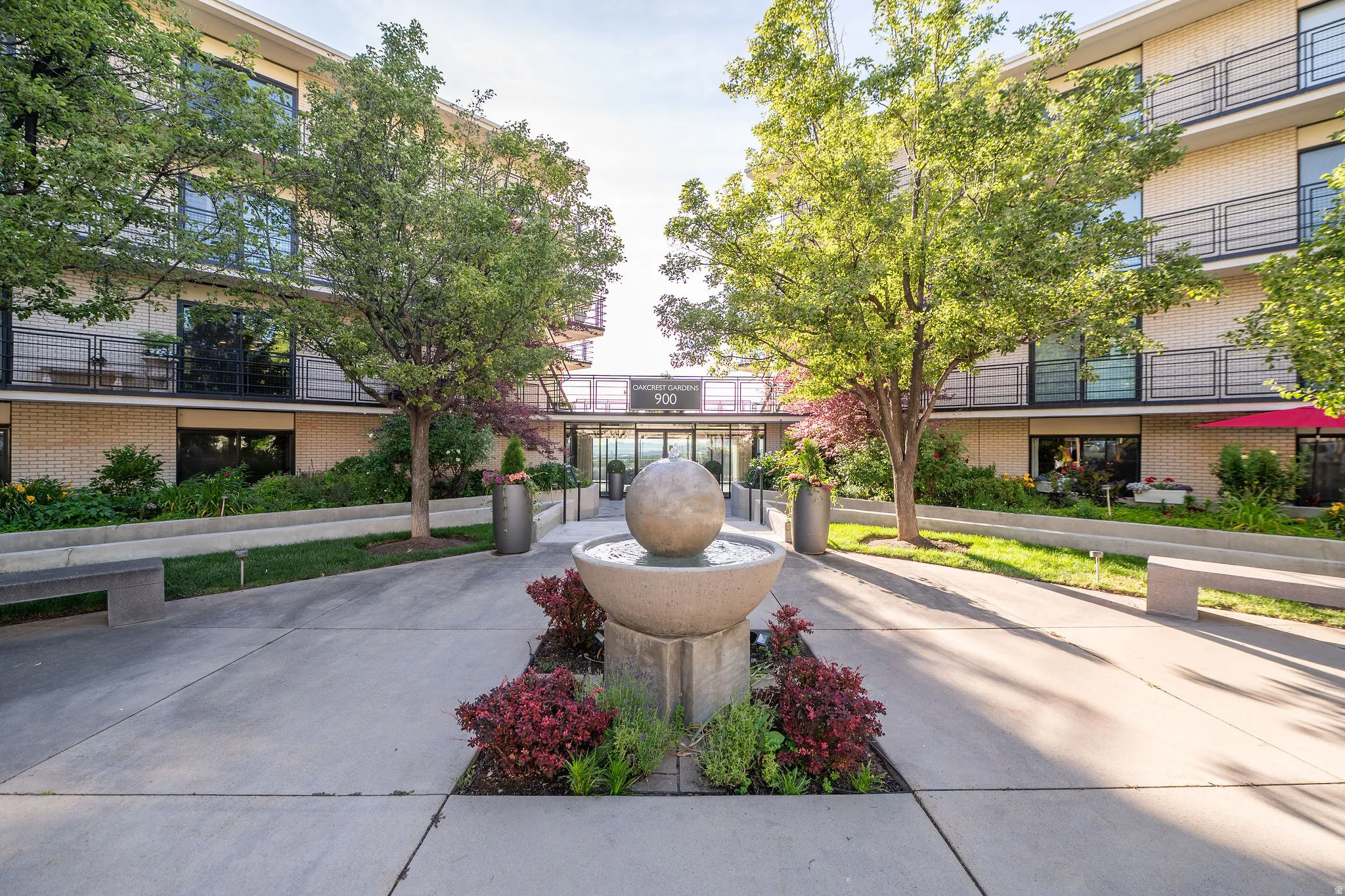 Modern building exterior featuring a central water feature, mature trees, concrete pathways, and integrated planters