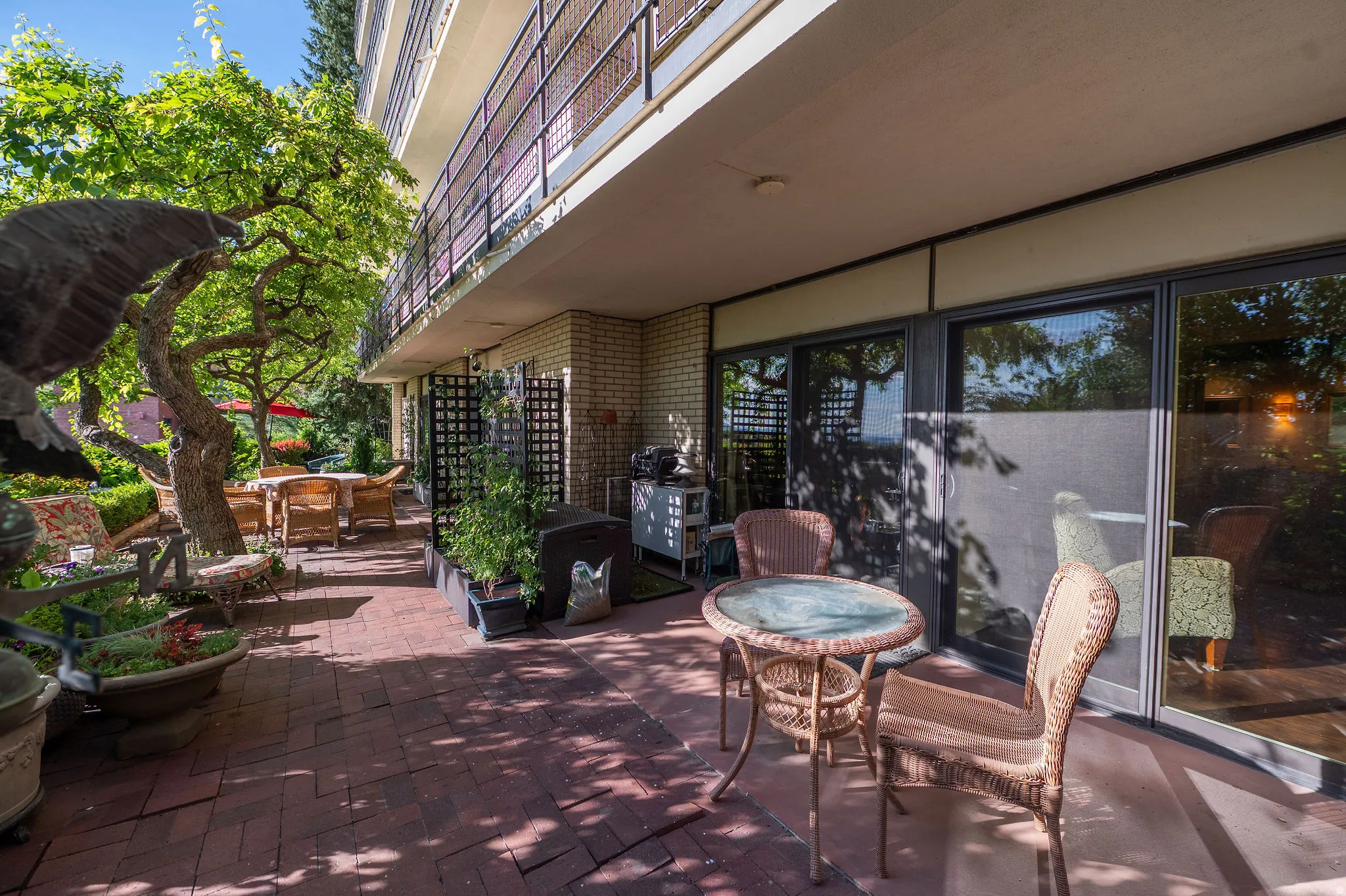 Expansive brick patio featuring mature landscaping, a covered outdoor area, and multiple sliding glass doors providing access to interior spaces