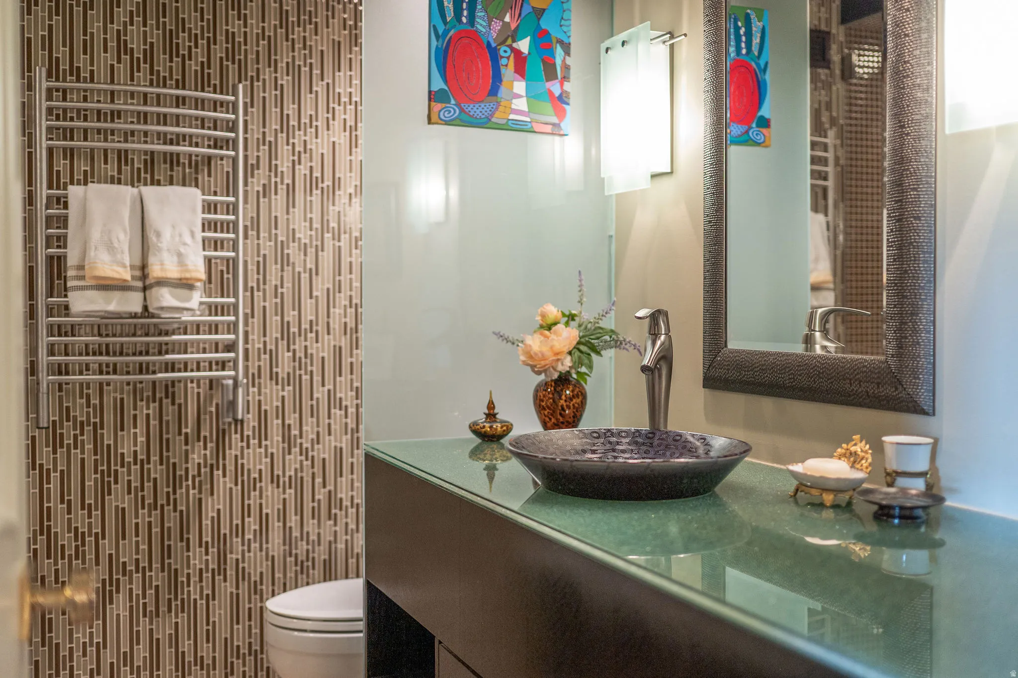 Contemporary bathroom vanity featuring a black vessel sink, glass countertop, and framed mirror