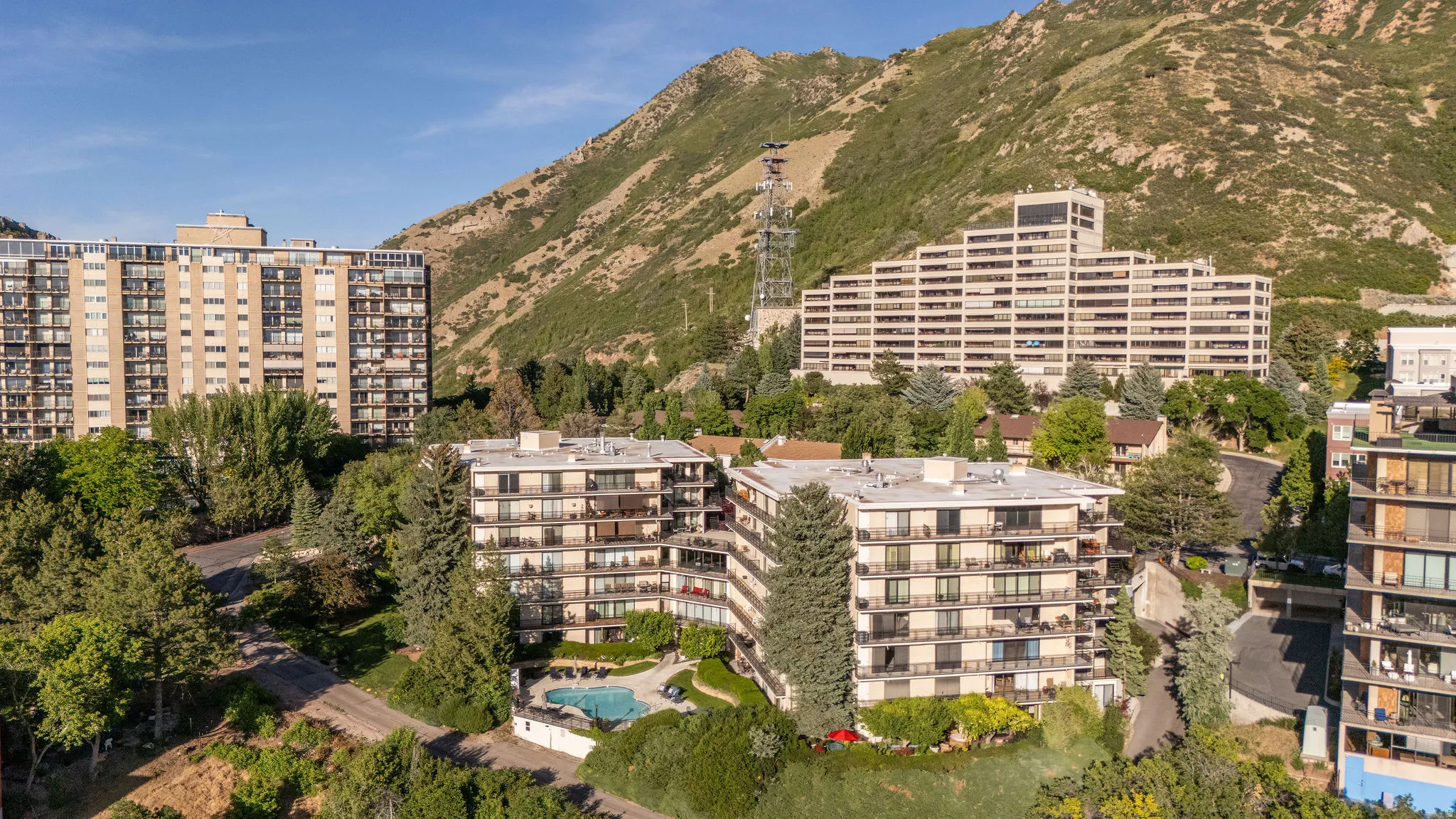 Community pool surrounded by mature landscaping and multi-story residential buildings set against a mountainous backdrop