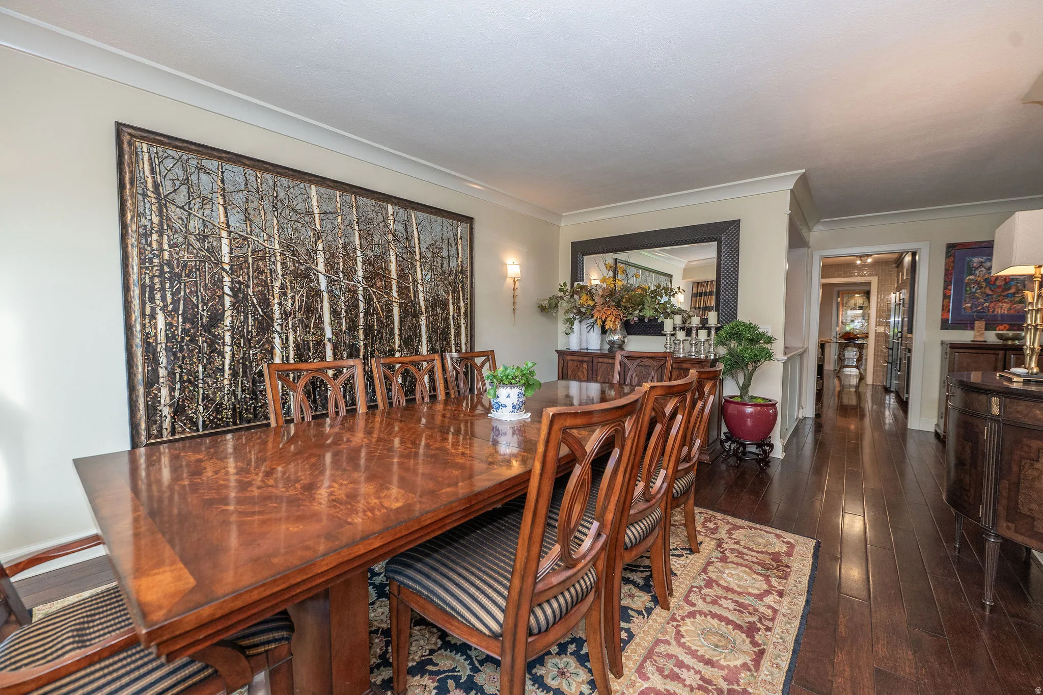 Formal dining area featuring rich wood-finish flooring, crown molding, and a wall-mounted sconce