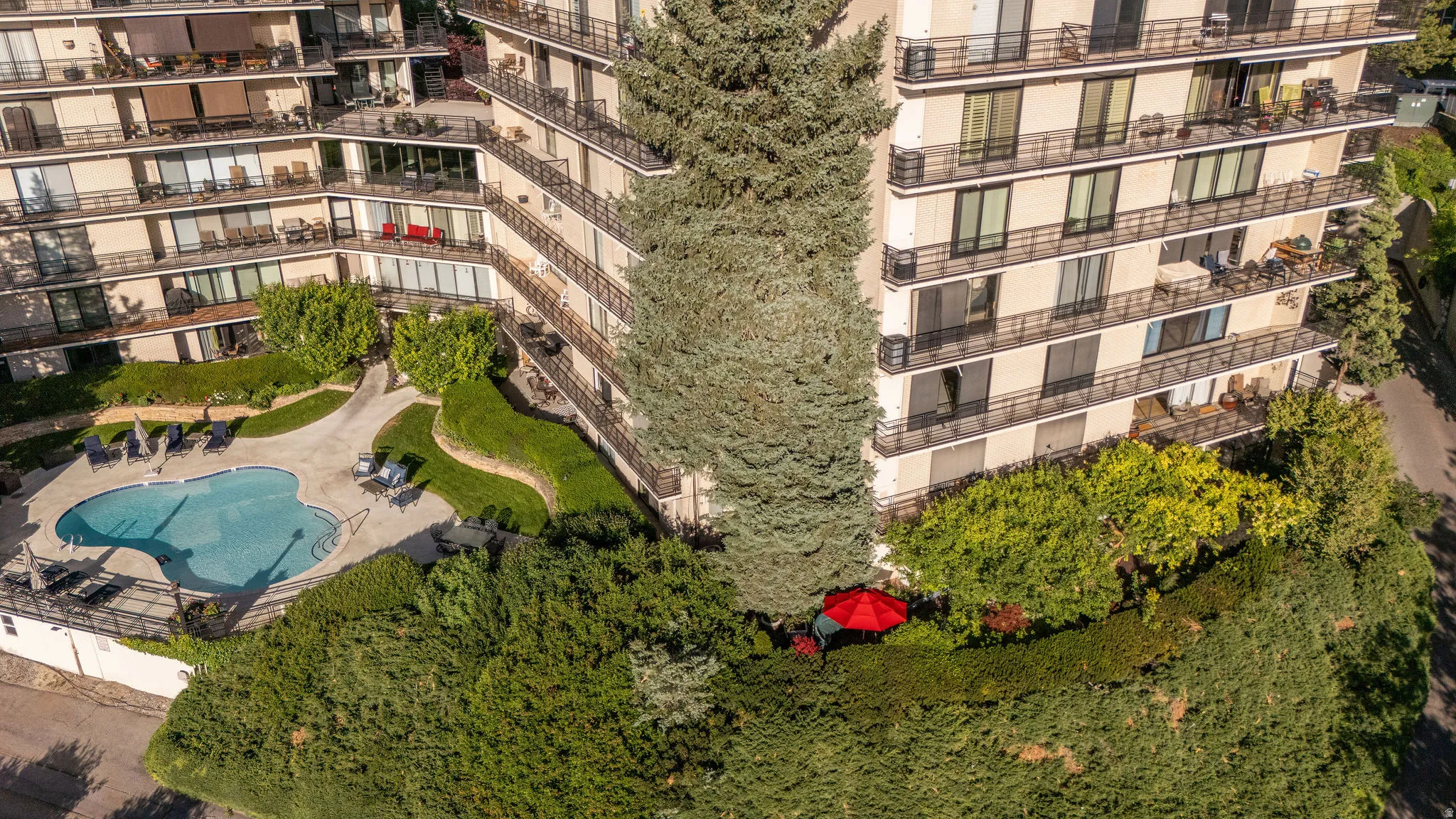 Multi-level apartment building featuring private balconies, extensive landscaping with mature trees, and an irregularly shaped swimming pool