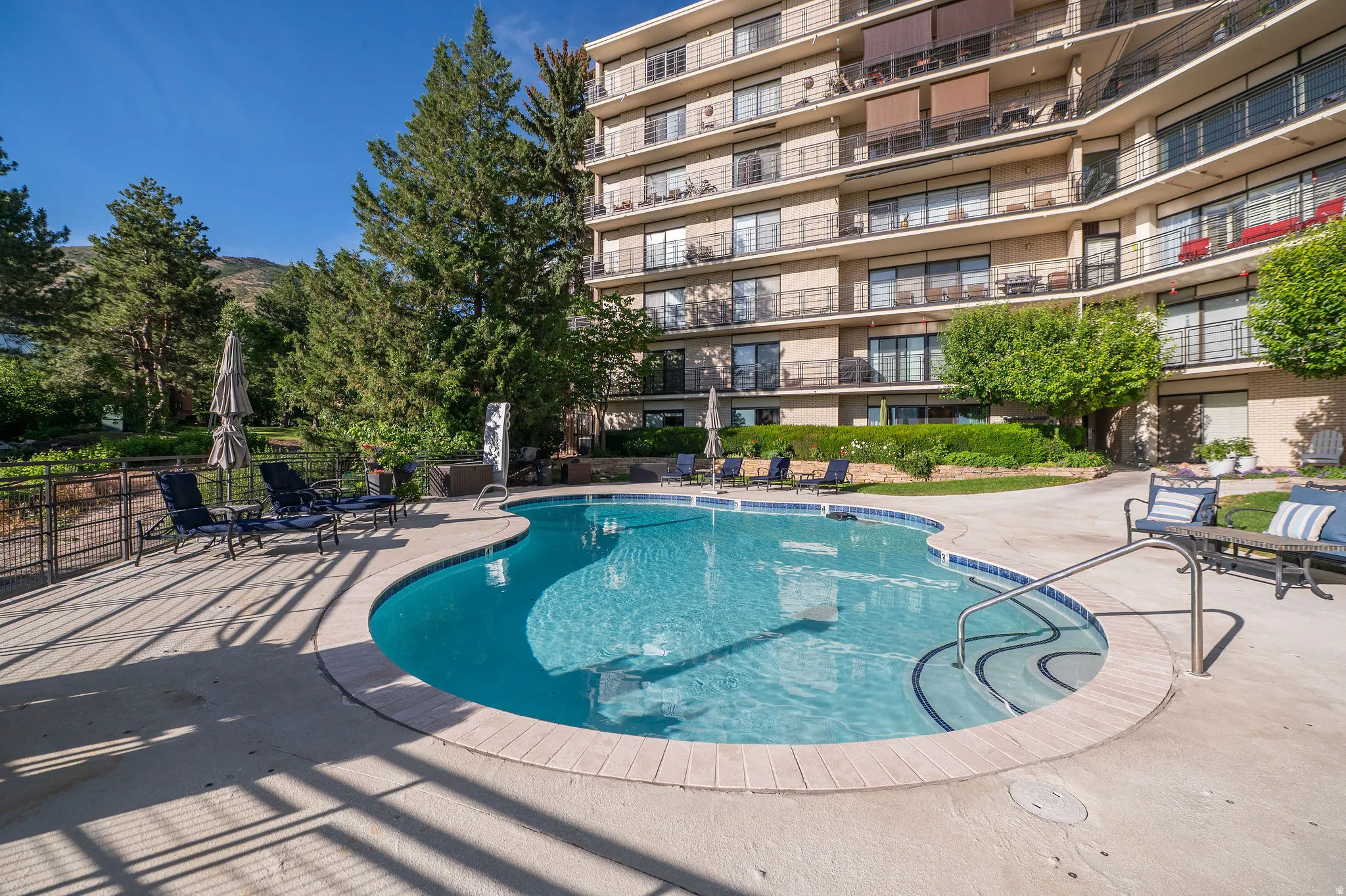 Outdoor swimming pool with integrated steps, surrounded by a concrete patio and lush landscaping
