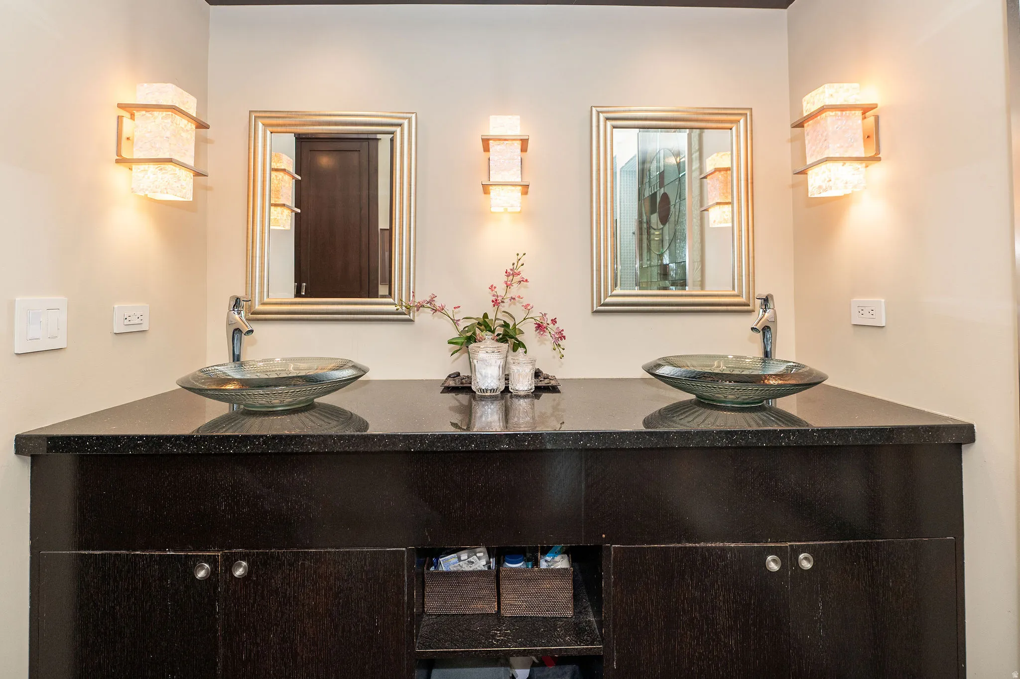 Dual vessel sinks set on a dark countertop with integrated cabinetry
