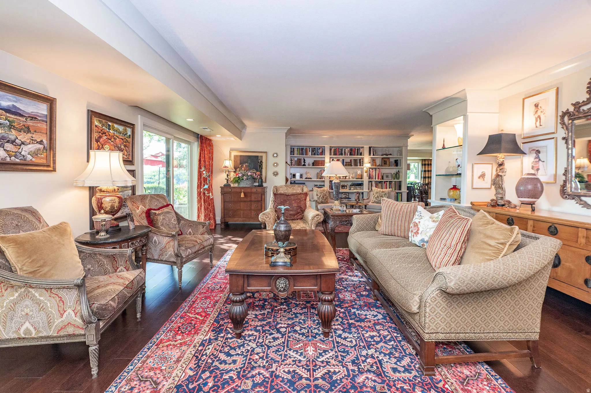 Spacious living area featuring dark wood-finish flooring, a large sliding glass door, recessed lighting, built-in shelving, and a decorative column