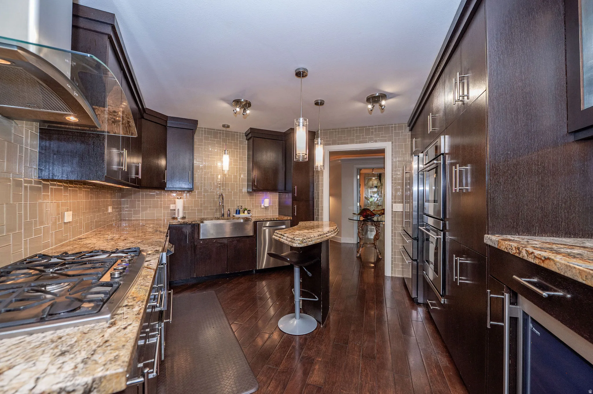 Gourmet kitchen featuring dark wood cabinetry, granite countertops, a stainless steel gas range with a curved glass hood, a farmhouse-style sink, and built-in double ovens