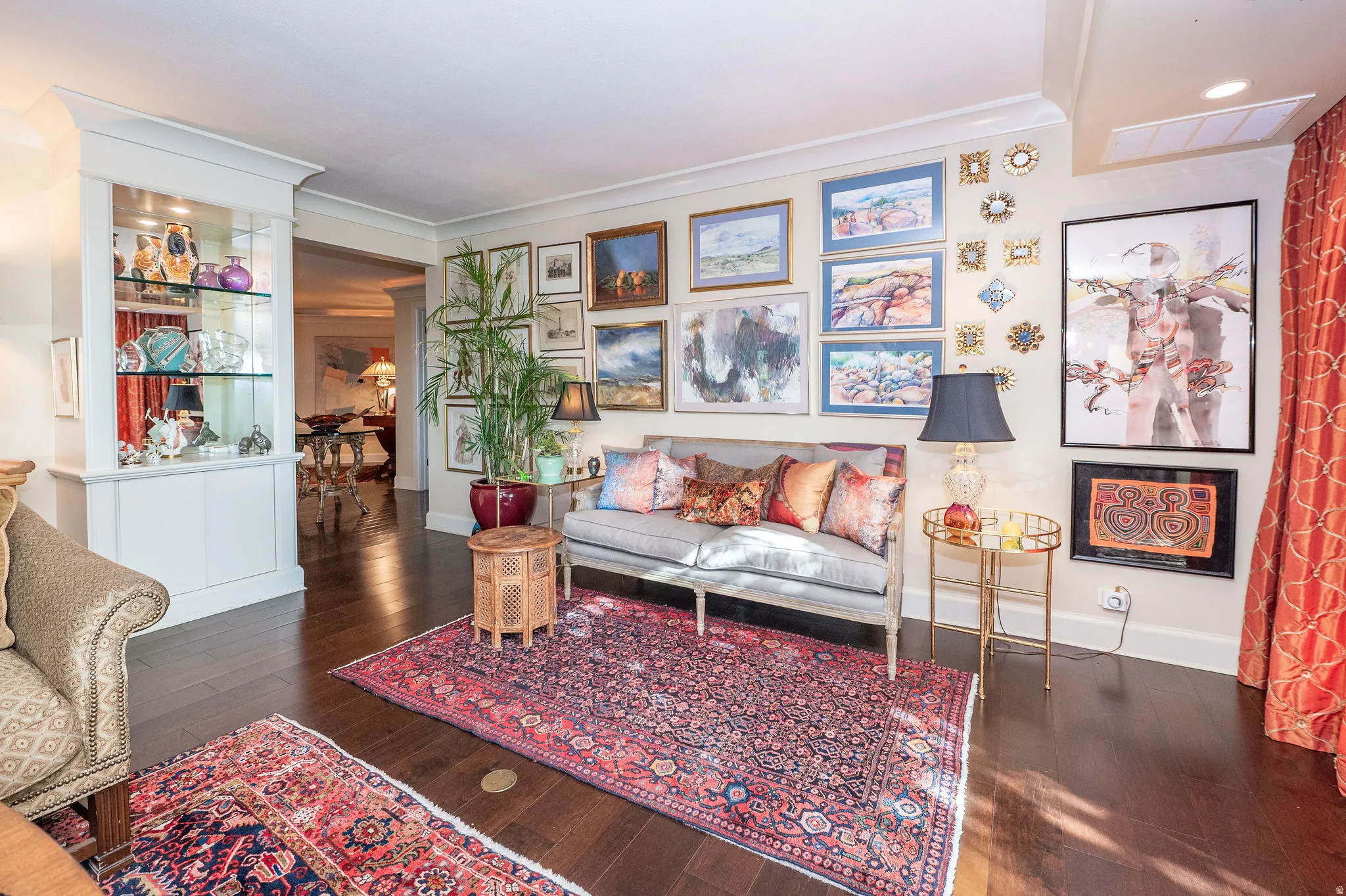Hardwood-finish flooring extending through an arched entryway, built-in display cabinetry with glass shelving, crown molding, and substantial baseboards