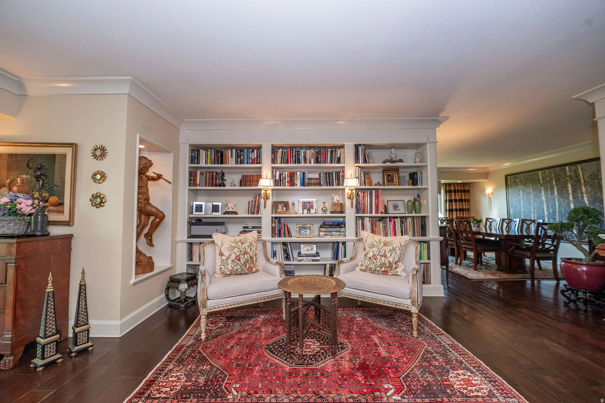 Built-in bookshelves with integrated sconce lighting, dark wood-finish flooring, crown molding, and a recessed wall niche