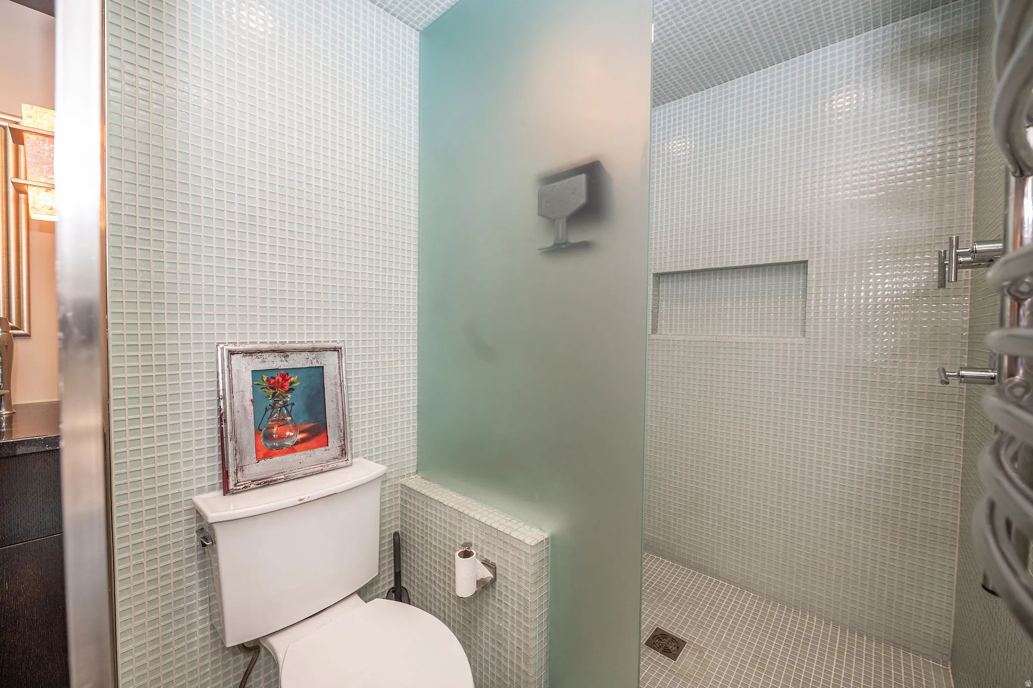 Shower area featuring full-height light-colored square mosaic tiling, built-in shower niche, and a glass privacy panel