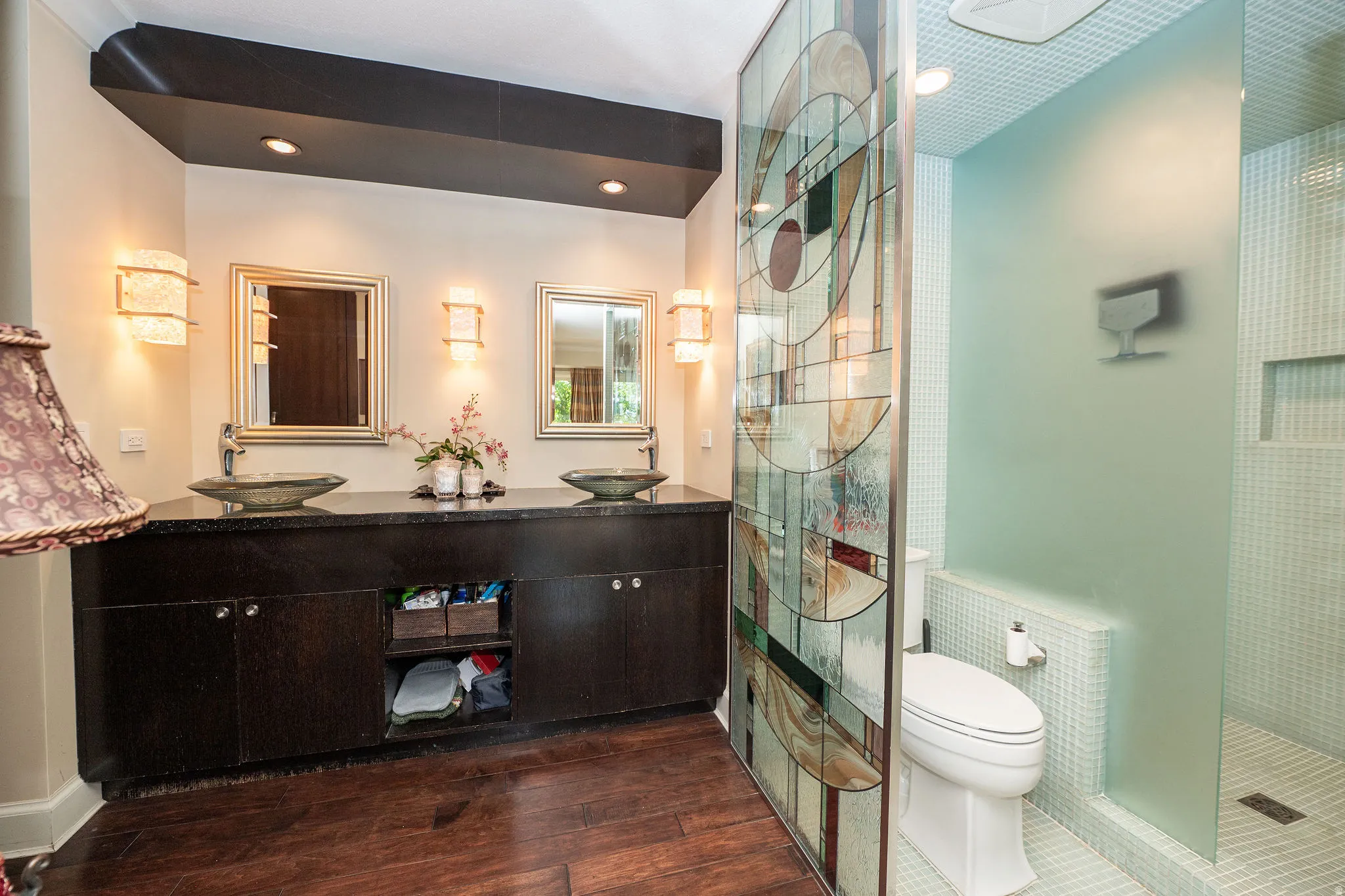 Dual vessel sinks set in a dark wood vanity with a stone countertop, framed mirrors, and sconce lighting