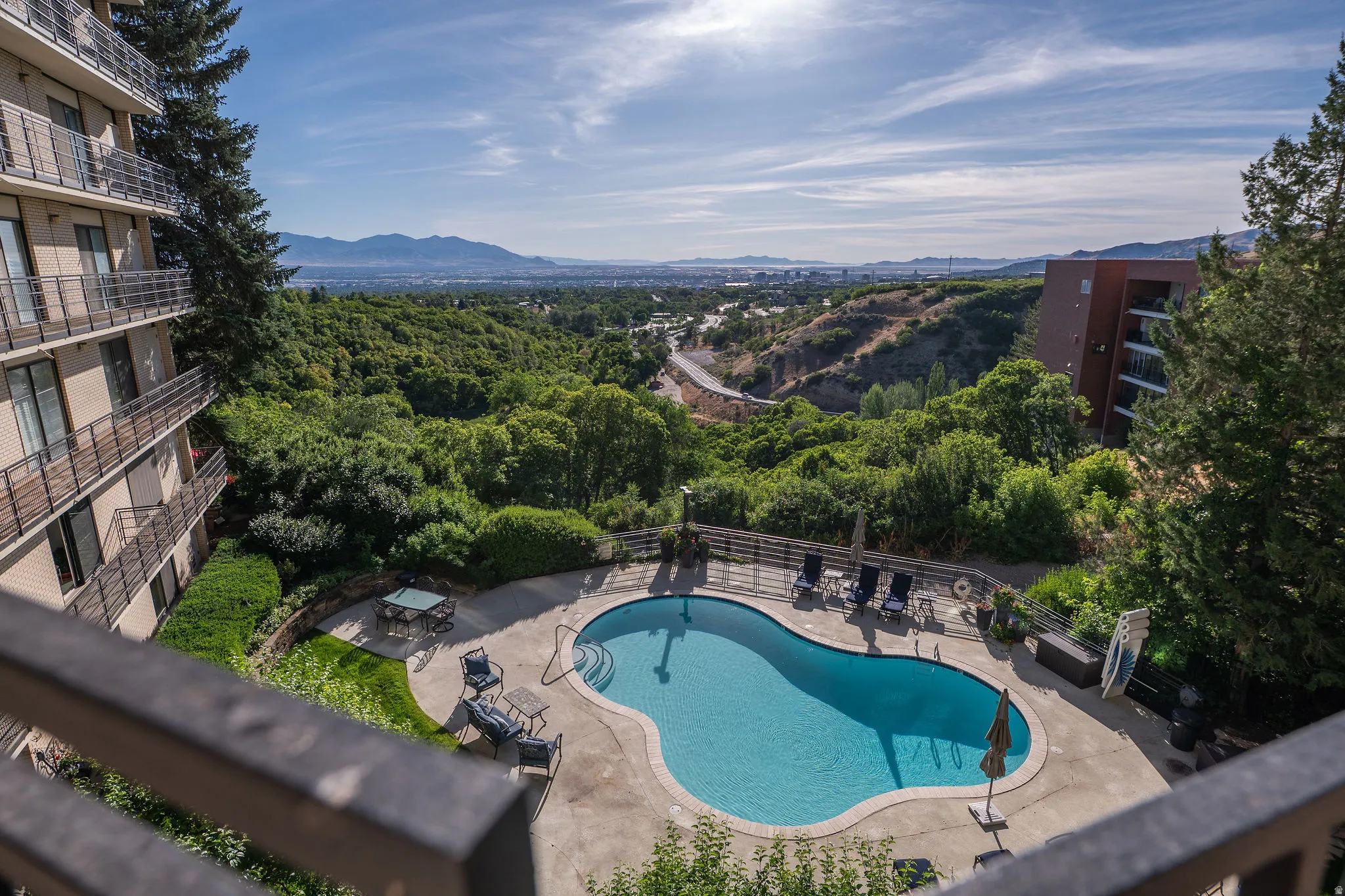 Resort-style pool area featuring a freeform swimming pool, surrounding concrete patio, and lush green landscaping