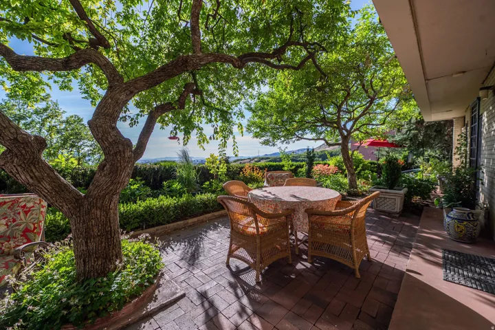 Brick paver patio shaded by mature trees, featuring manicured hedges and distant landscape