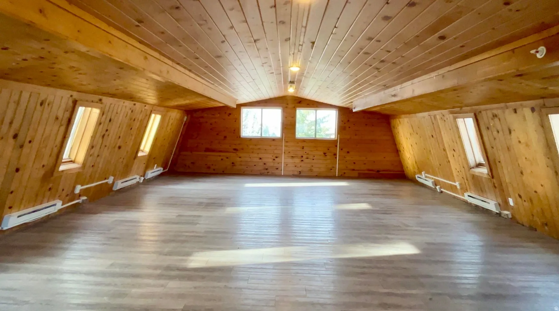 Expansive attic space featuring wood-paneled walls and ceiling, multiple skylights, and light wood-finish flooring