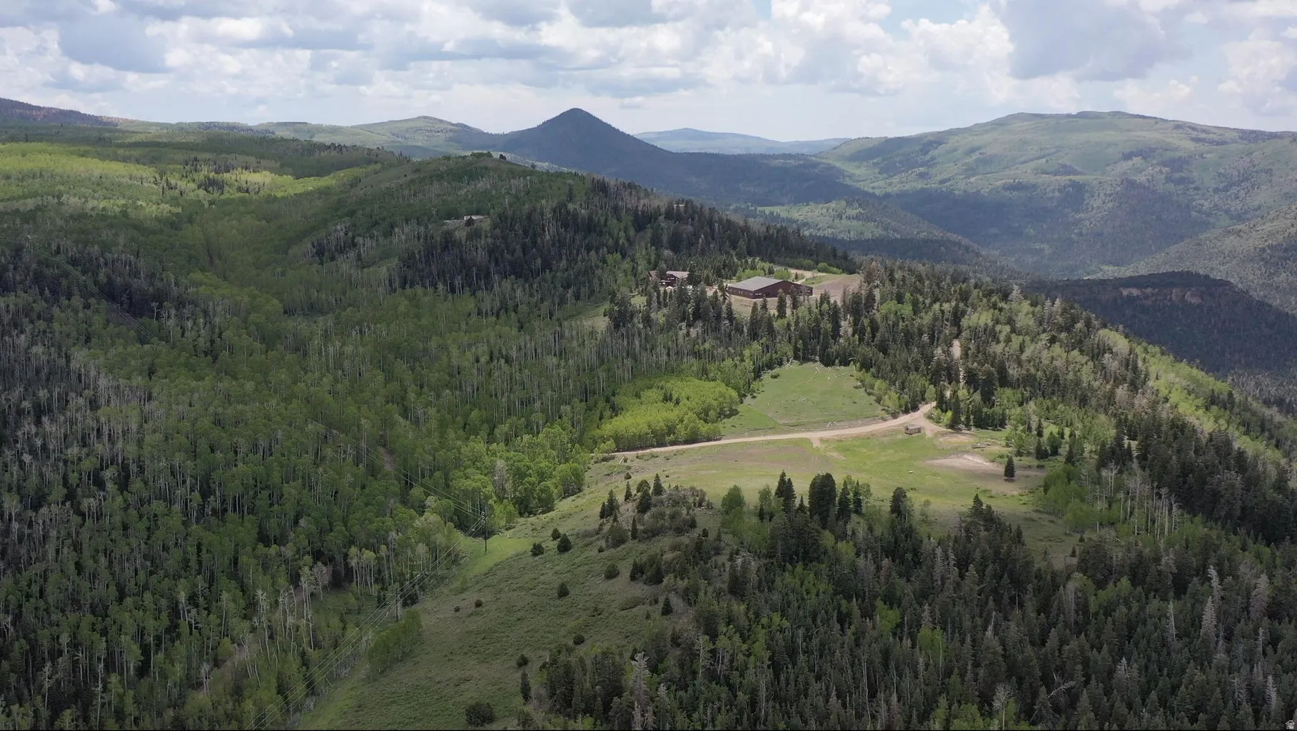 Expansive acreage with established structures, surrounded by dense forestation and open clearings