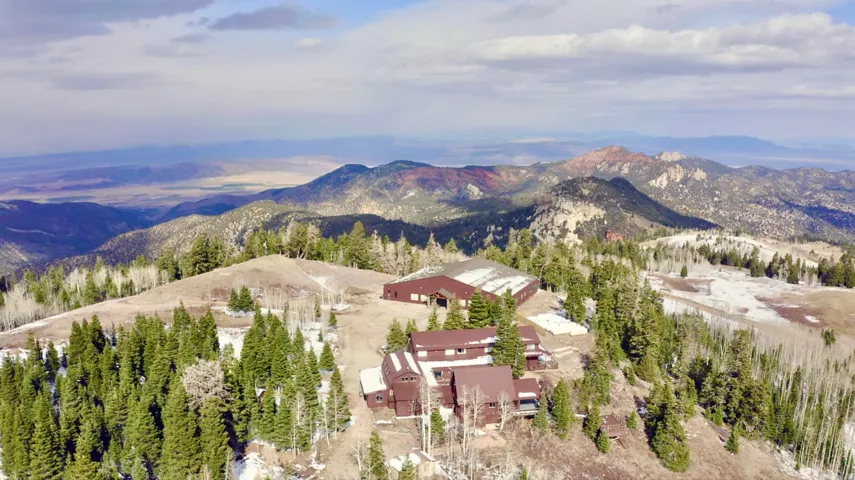 Expansive mountain property featuring multiple structures, surrounded by evergreen forests and distant mountain ranges