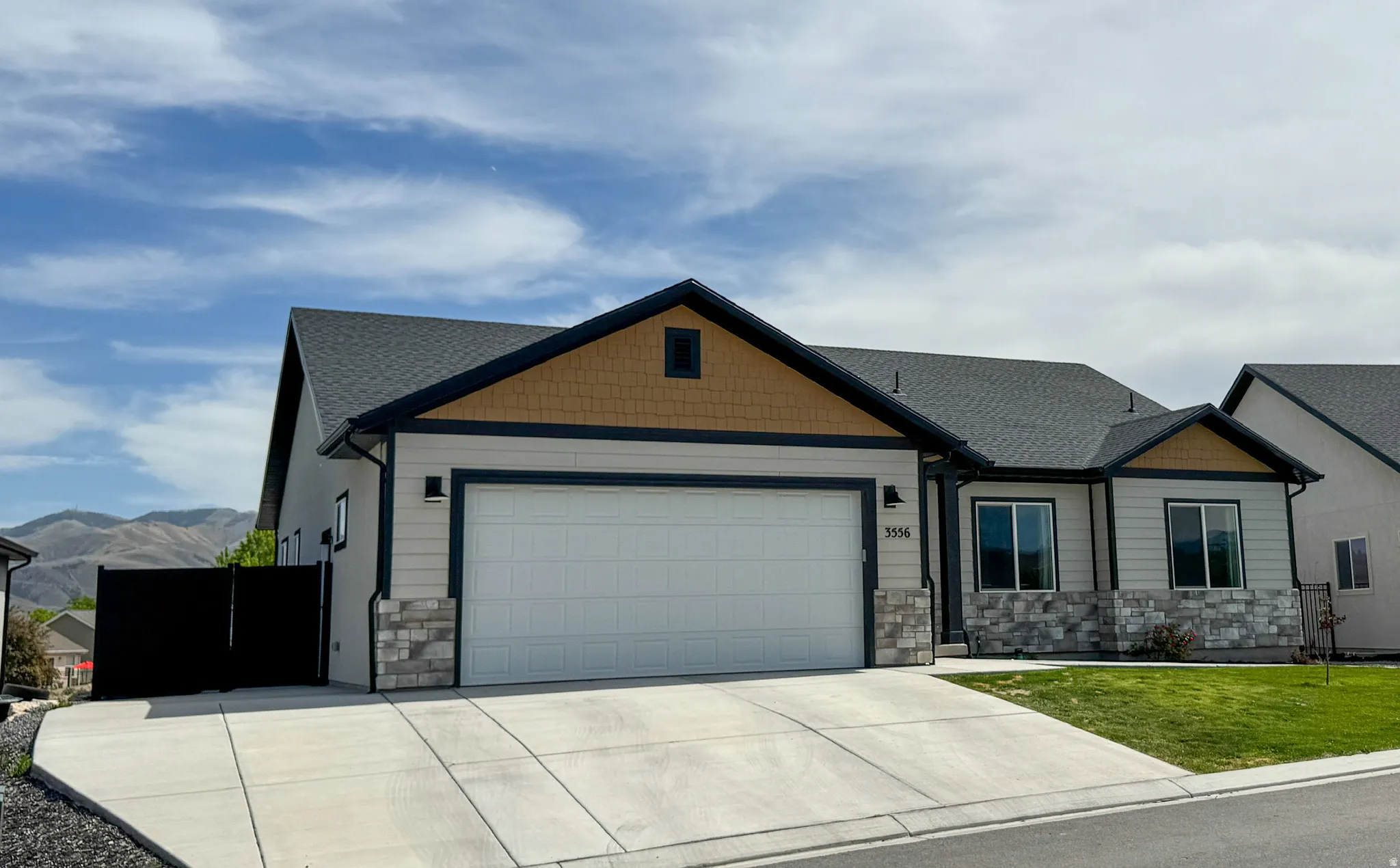 Contemporary single-story residence featuring a two-car garage, stone veneer accents, and a dark asphalt shingle roof