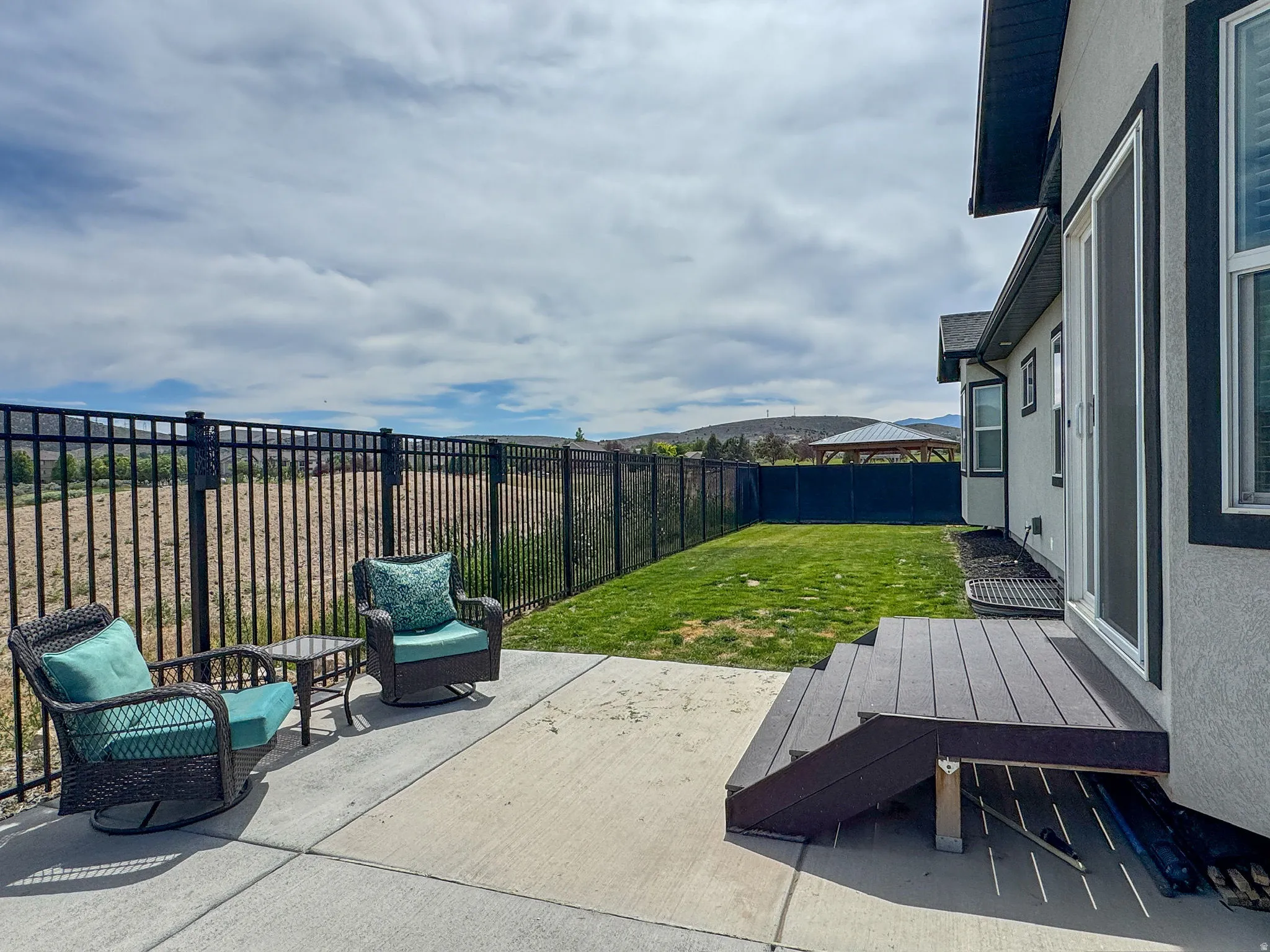 Backyard patio featuring a concrete surface, black metal fencing, a small lawn area, and a composite deck with stairs