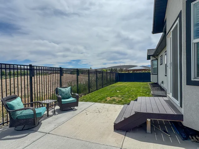 Backyard patio featuring a concrete surface, black metal fencing, a small lawn area, and a composite deck with stairs