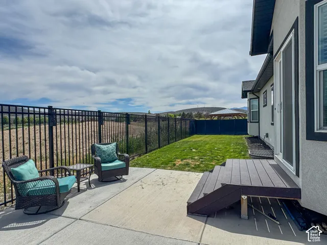 Backyard patio featuring a concrete surface, black metal fencing, a small lawn area, and a composite deck with stairs