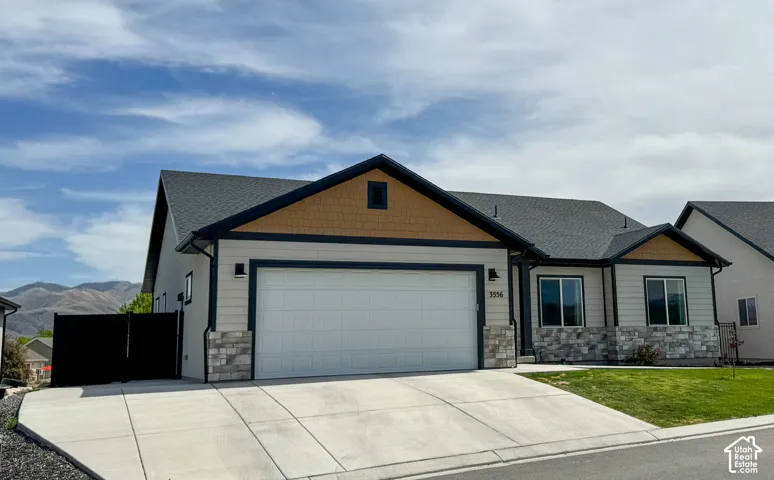 Contemporary single-story residence featuring a two-car garage, stone veneer accents, and a dark asphalt shingle roof