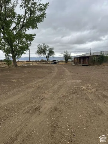 Expansive open lot with distant mountains, mature trees, and a single-story structure