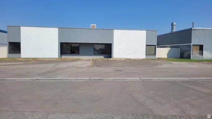 Commercial building with a gray and white exterior facade, featuring multiple window openings and a paved parking area