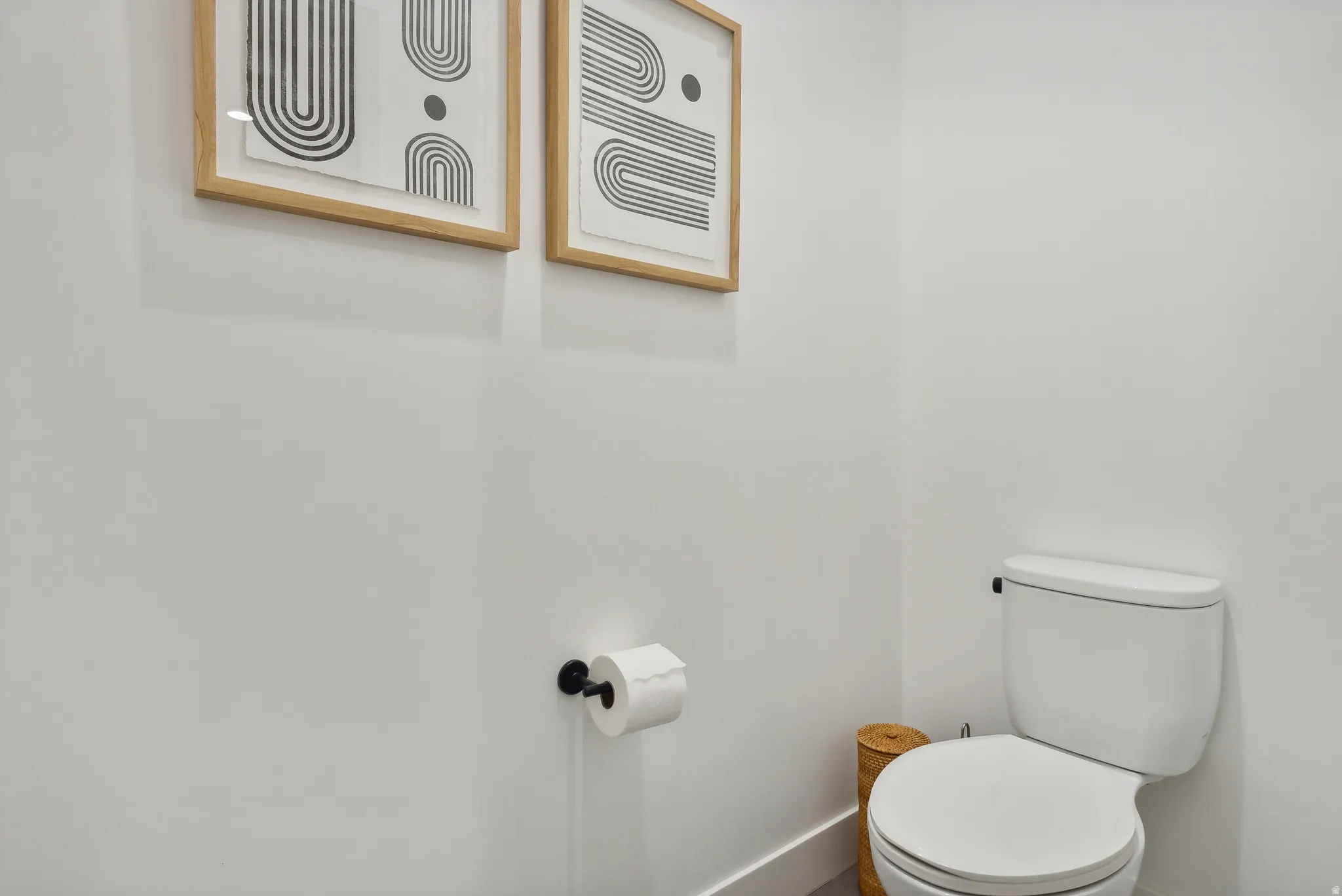 White toilet with a black flush handle, black wall-mounted toilet paper holder, and white baseboards