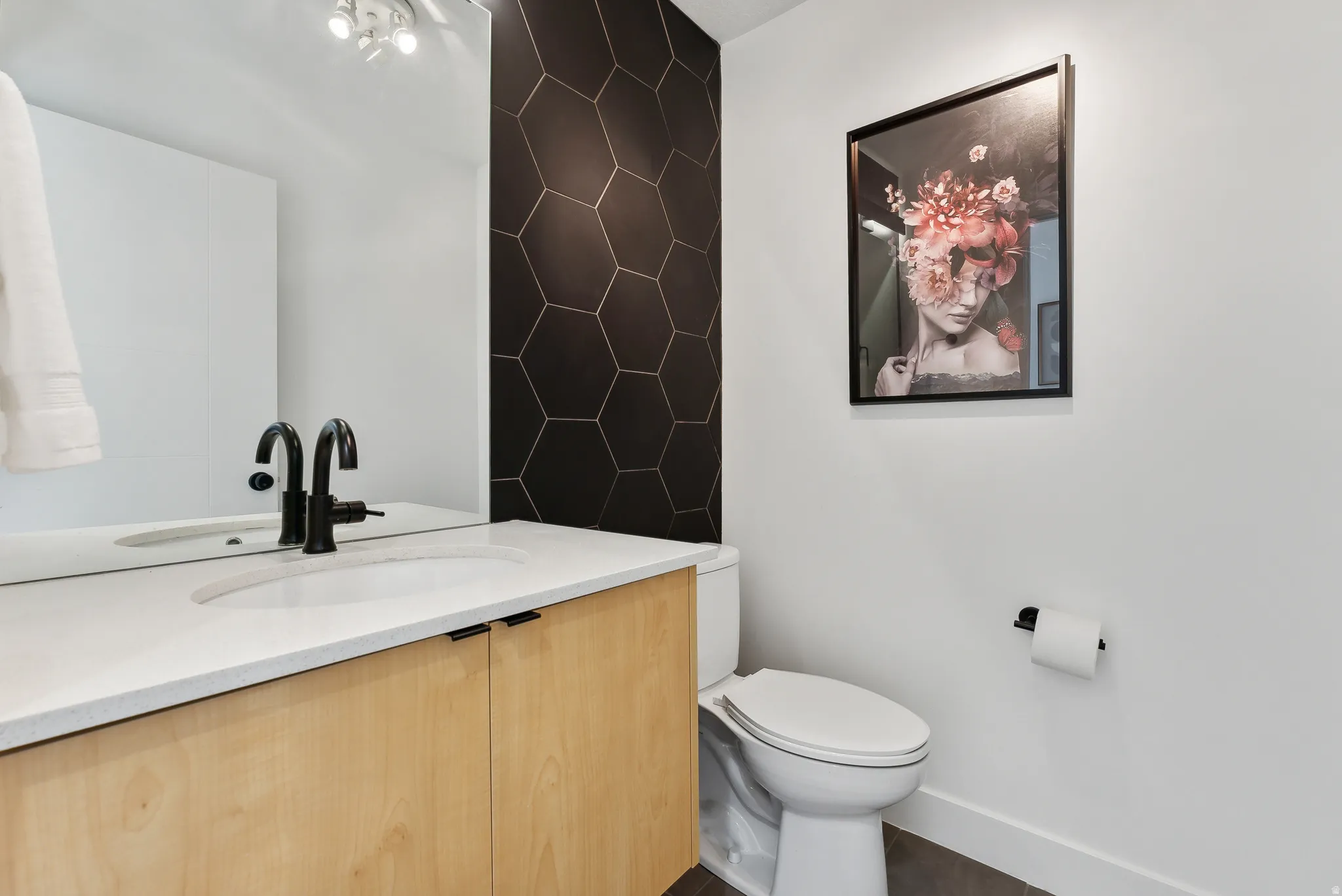 Bathroom vanity featuring a light wood-finish cabinet with black hardware, a light-toned countertop, and an integrated sink with a matte black faucet
