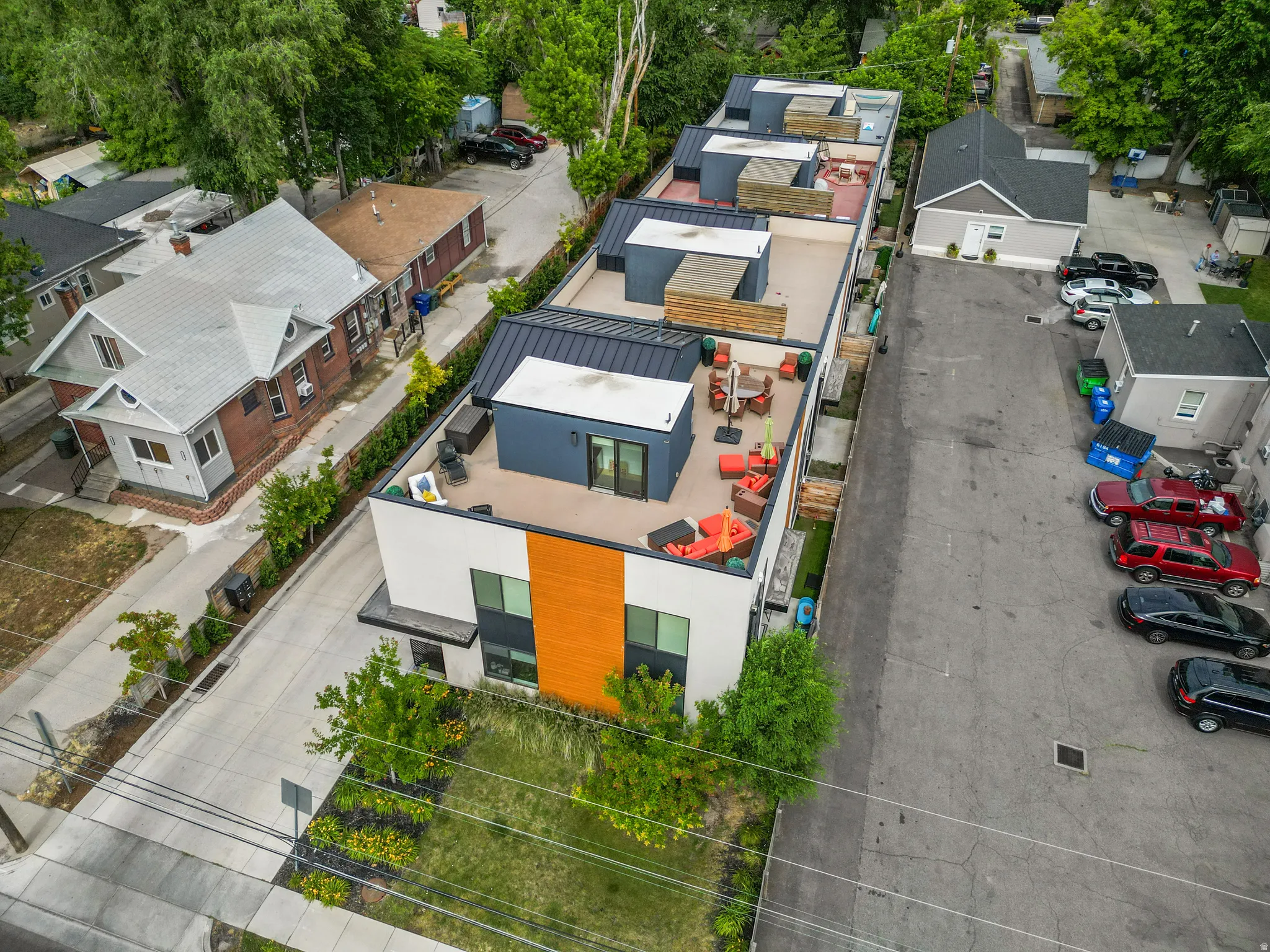Contemporary multi-level residence featuring a flat roofline with multiple rooftop deck spaces, a white and wood-tone exterior, and an expansive paved parking area