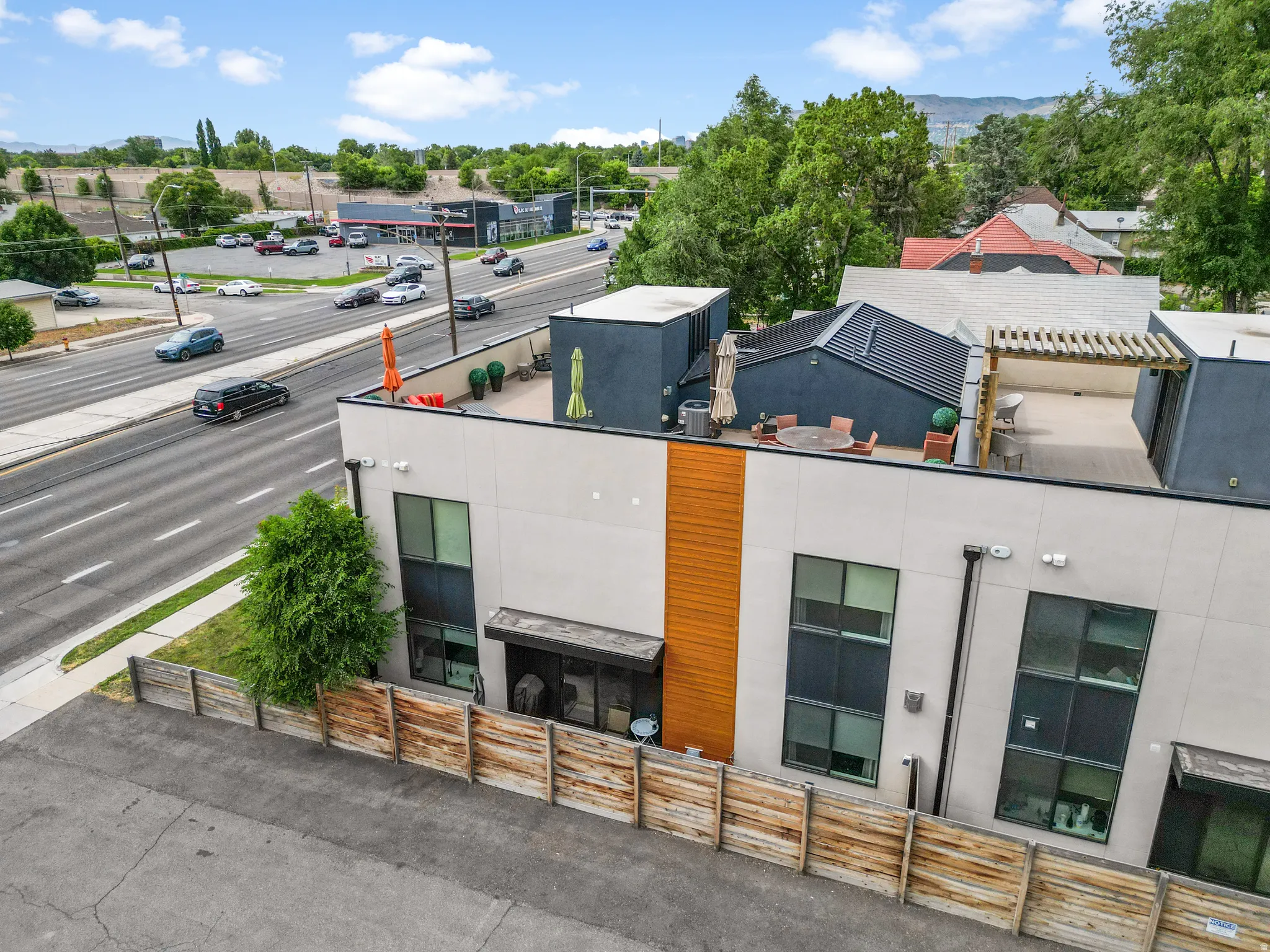 Modern building exterior featuring a rooftop deck with a pergola, contemporary siding, large windows, and an adjacent street