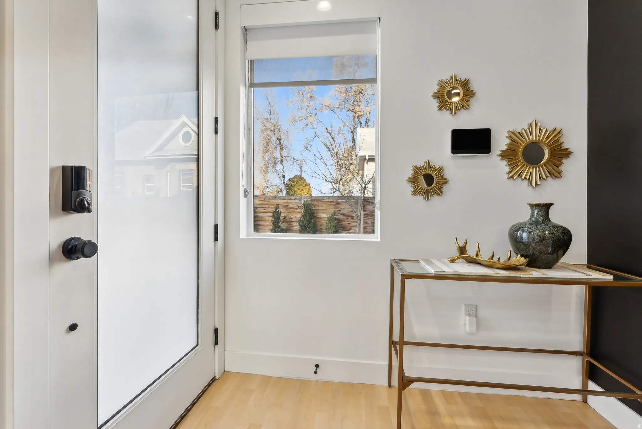 Entryway featuring a frosted glass door, smart lock, wood-finish flooring, and a large window with roller shade